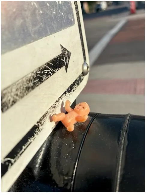 Photo of a street sign with a tiny plastic baby underneath it.